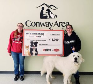 Two CAHS adoption counselors stand with a dog and an oversized $5000 check to signify our recognition as a top shelter.